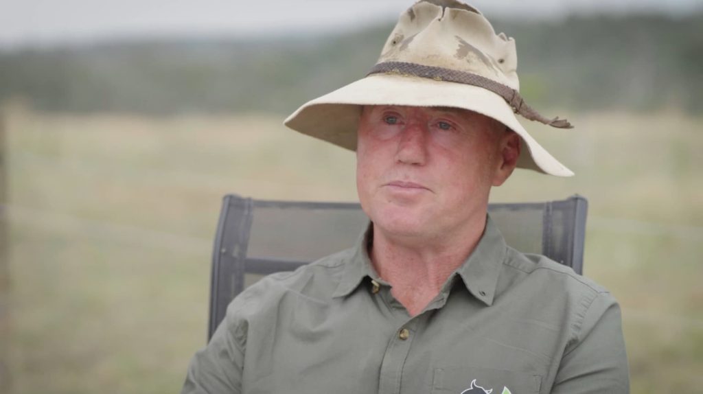 Close up of a man wearing a cream-coloured, broad brimmed hat and green button up shirt.