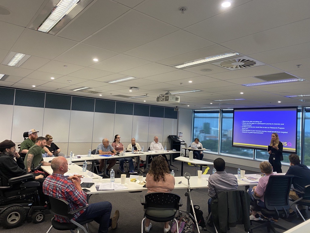 Image of a meeting room with participant reference group looking at a presenter from the NIISQ Agency