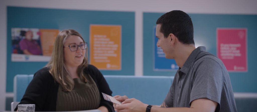 A man and a woman sit at a table talking.