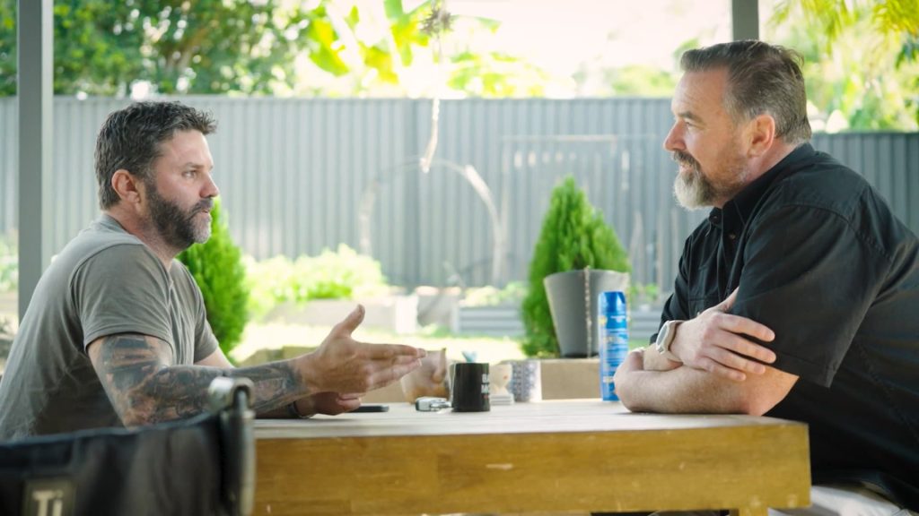 Two men sit across from each other at a table talking.