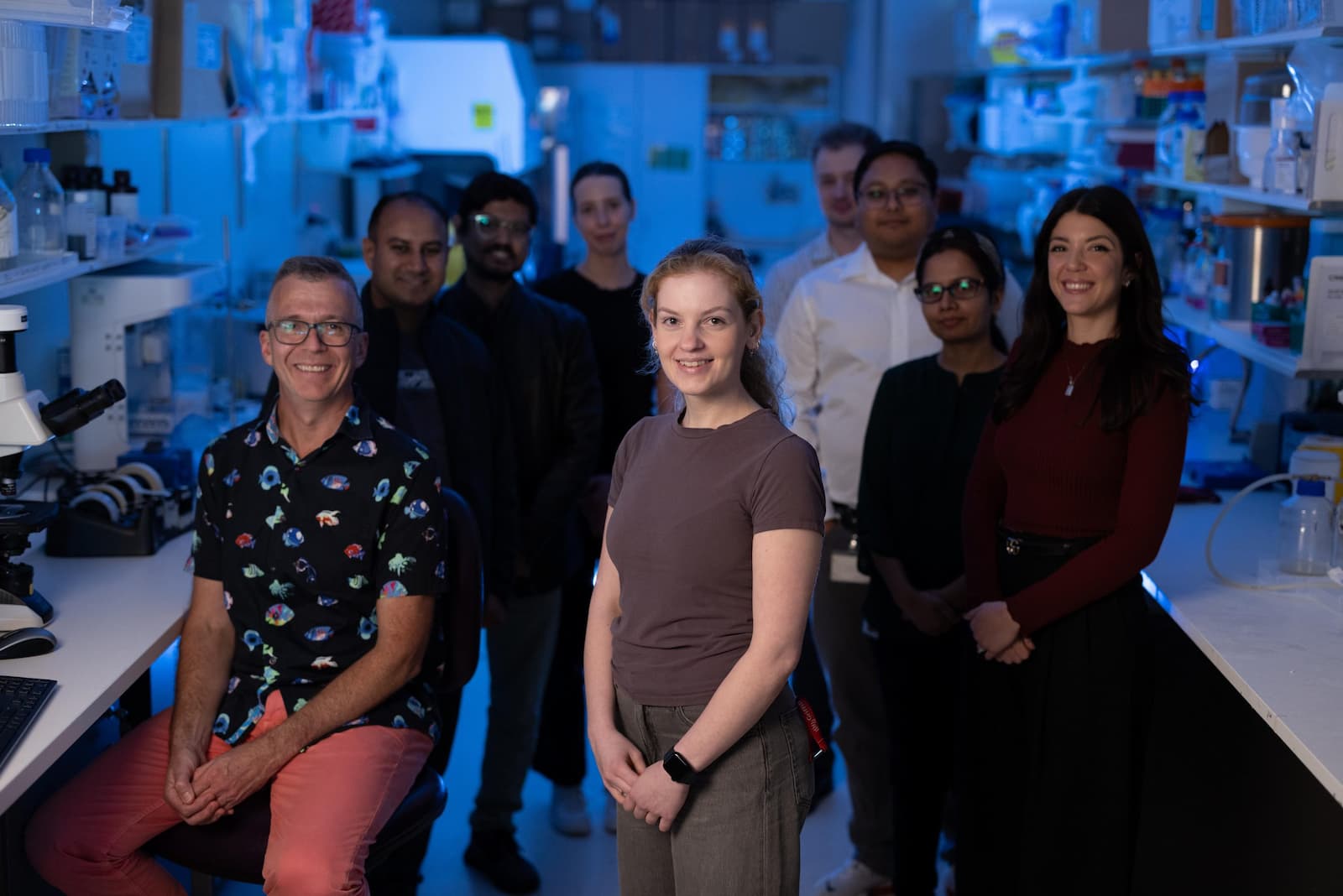 A group of 8 smiling people stand together in a lab.